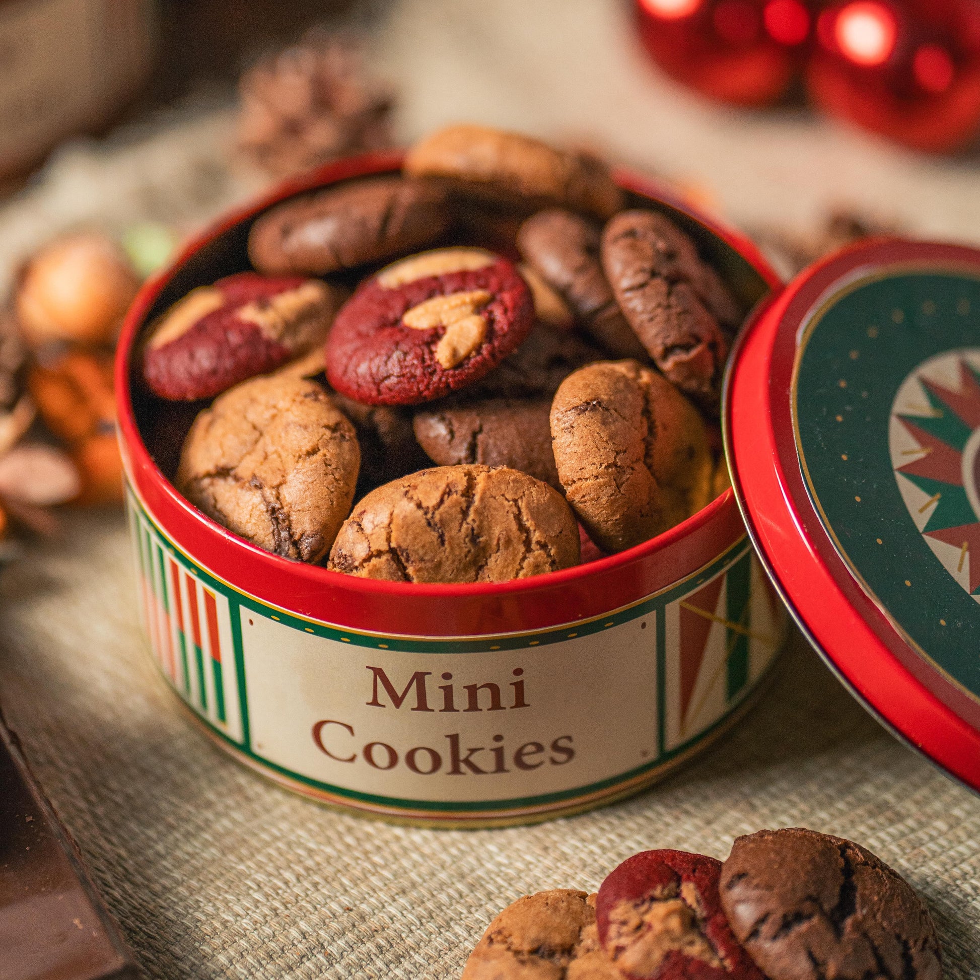 Mini cookies in a decorative tin with Christmas ornaments in the background