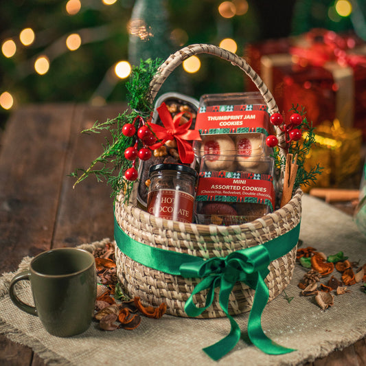 Gift basket with cookies and a mug on a wooden surface with Christmas decorations in the background.