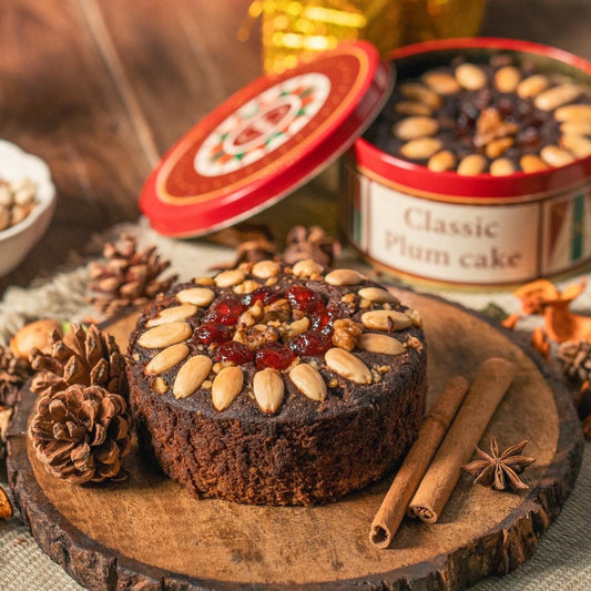 Fruitcake with nuts and jam on a wooden board with 'Classic Plum Cake' tins in the background.